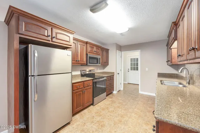 a kitchen with stainless steel appliances granite countertop a refrigerator a stove and a sink