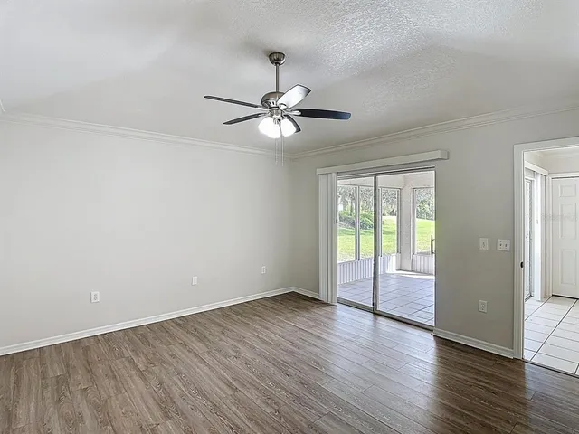 a view of an empty room with wooden floor and a ceiling fan