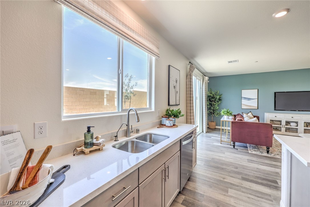 1017 Copper Robin Street Henderson, NV 89011 - Photo 43 of 43 Kitchen with a sink, stainless steel dishwasher, light countertops, light. wood-type flooring, and open floor plan. Photo is representational only; actual home finishes may vary.