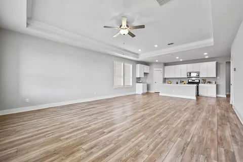 a view of an empty room and kitchen view with wooden floor