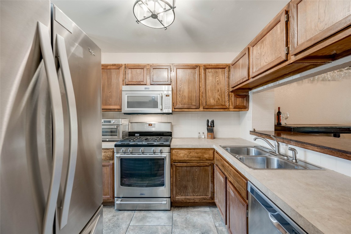11821 Bittern Hollow, Unit 34 Austin, TX 78758 - Photo 11 of 24 Kitchen featuring appliances with stainless steel finishes, light countertops, tasteful backsplash, light tile patterned floors, and brown cabinets