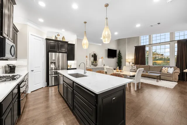 a large kitchen with stainless steel appliances a large counter top a stove a refrigerator and a view of living room