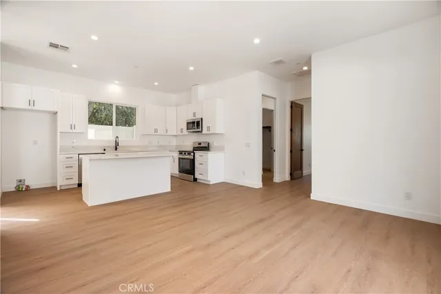 a view of kitchen with stainless steel appliances refrigerator oven and white cabinets with wooden floor