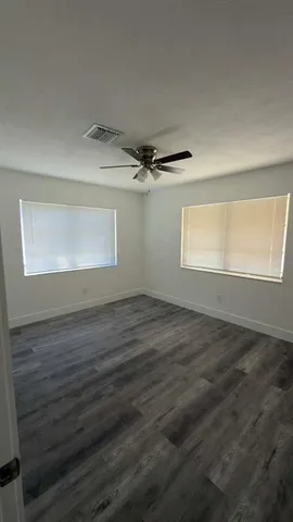 an empty room with wooden floor fan and windows
