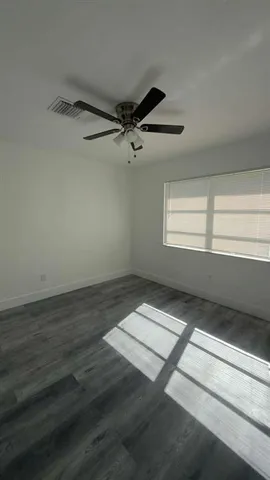 an empty room with wooden floor fan and windows