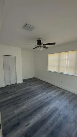 an empty room with wooden floor fan and windows