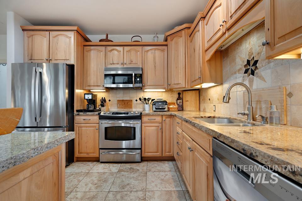 7025 Bluebird Lane Sweet, ID 83670 - Photo 18 of 46 Kitchen with stainless steel appliances, backsplash, light brown cabinetry, and light stone counters