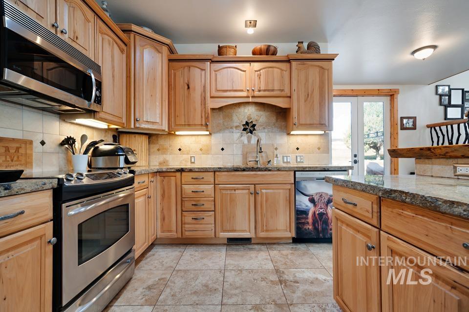 7025 Bluebird Lane Sweet, ID 83670 - Photo 21 of 46 Kitchen featuring stainless steel appliances, decorative backsplash, dark stone counters, light brown cabinets, and french doors