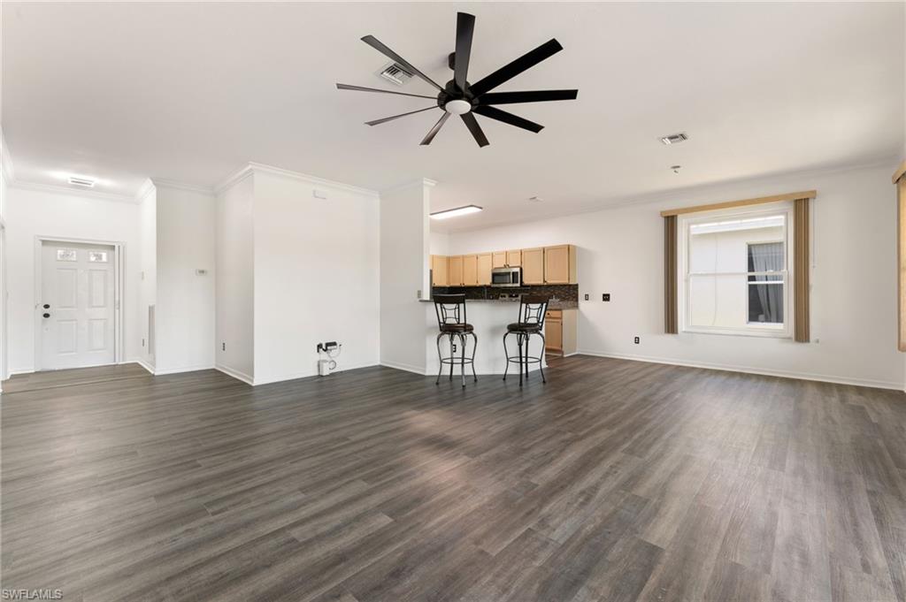 223 Stanhope Circle Naples, FL 34104 - Photo 7 of 41 Spacious room featuring wood-finish flooring, a contemporary ceiling fan, and a kitchen alcove with light wood cabinetry and dark countertops