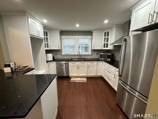 a kitchen with stainless steel appliances a refrigerator a sink a stove a refrigerator white cabinets and wooden floor