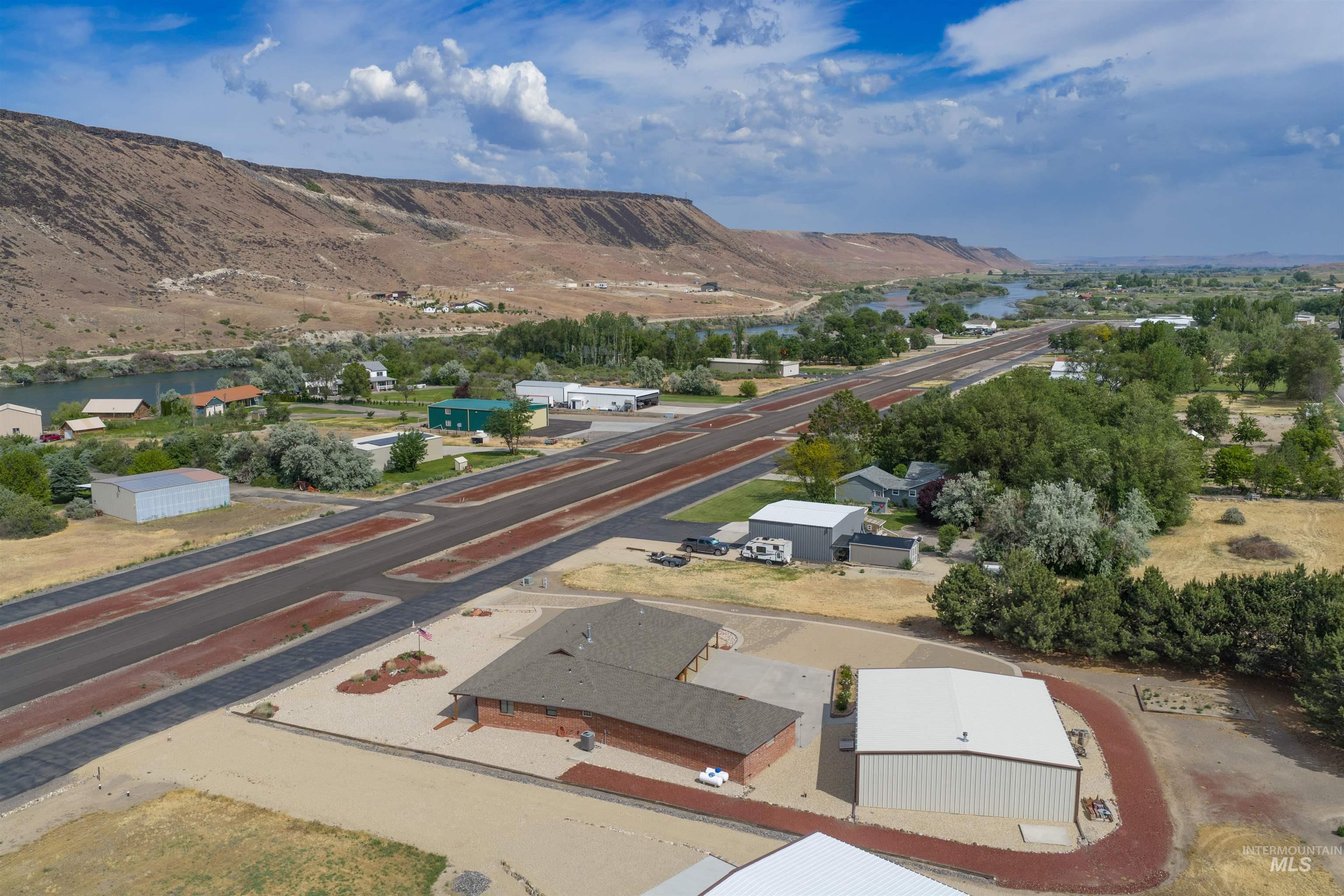 10514 Airpark Loop Road Melba, ID 83641 - Photo 40 of 47 Aerial perspective showcasing a single-story brick structure with a dark shingle roof, a large metal building with a white roof, and an expansive gravel lot
