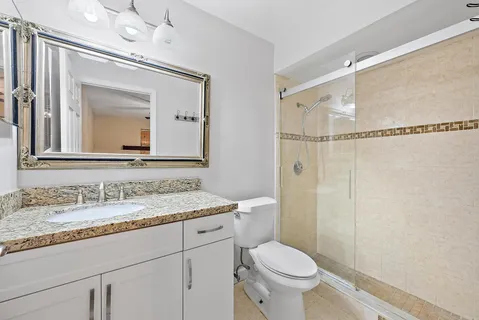 a bathroom with a granite countertop sink toilet mirror and a shower