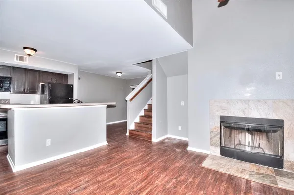 a view of a kitchen and an empty room with wooden floor and a fireplace