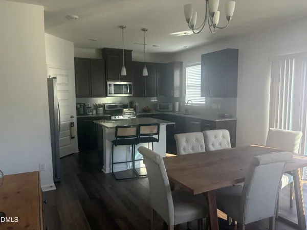 a kitchen with stainless steel appliances granite countertop a stove a refrigerator a sink a dining table and chairs with wooden floor