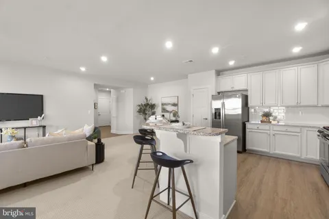 a living room with stainless steel appliances furniture a flat screen tv and a kitchen view