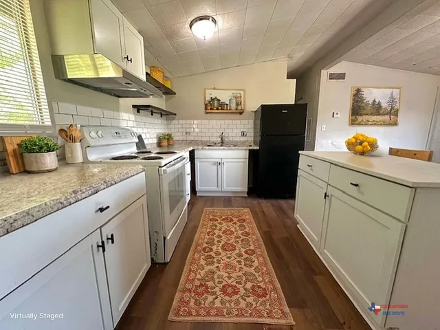 a kitchen with granite countertop stainless steel appliances a stove a sink a refrigerator white cabinets and wooden floor