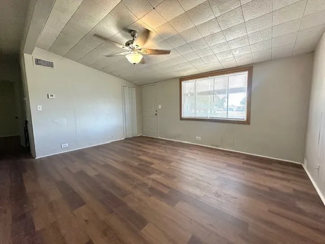 an empty room with wooden floor fan and windows