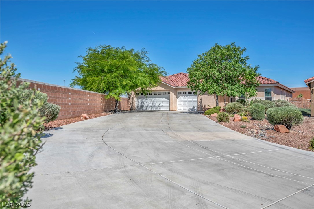 6405 North Raptor Court North Las Vegas, NV 89084 - Photo 54 of 66 A spacious driveway leads to a charming stucco residence, framed by vibrant green trees and desert landscaping.