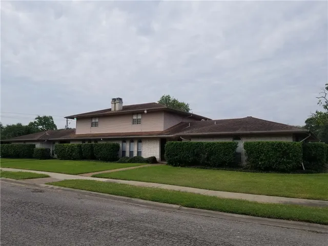 a view of a big house in front of a big yard with plants and large trees