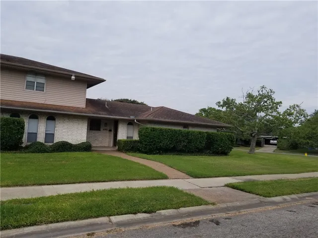 a brick house with a yard plants and big trees
