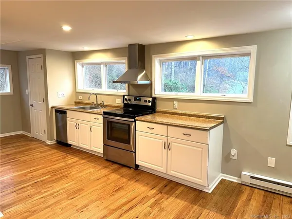 a kitchen with stainless steel appliances granite countertop a stove a sink and white cabinets with wooden floor