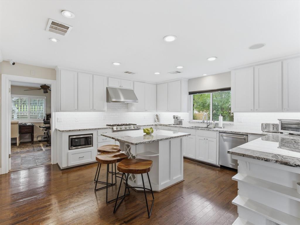 6160 Spring Valley Road Dallas, TX 75240 - Photo 11 of 40 White cabinetry kitchen with granite countertops, stainless steel appliances, a center island, and wood-finish flooring