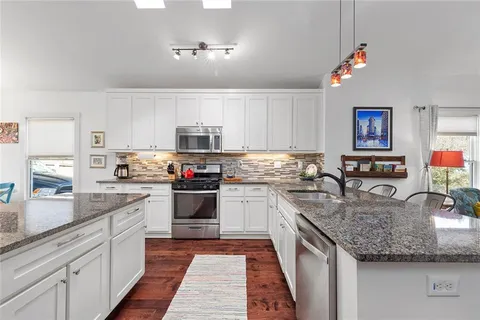 a kitchen with stainless steel appliances granite countertop a refrigerator a stove top oven a sink dishwasher and white cabinets with wooden floor