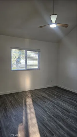 a view of an empty room with wooden floor and a kitchen