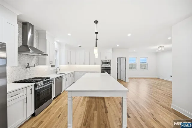 a large kitchen with kitchen island a stove a sink a refrigerator and white cabinets with wooden floor