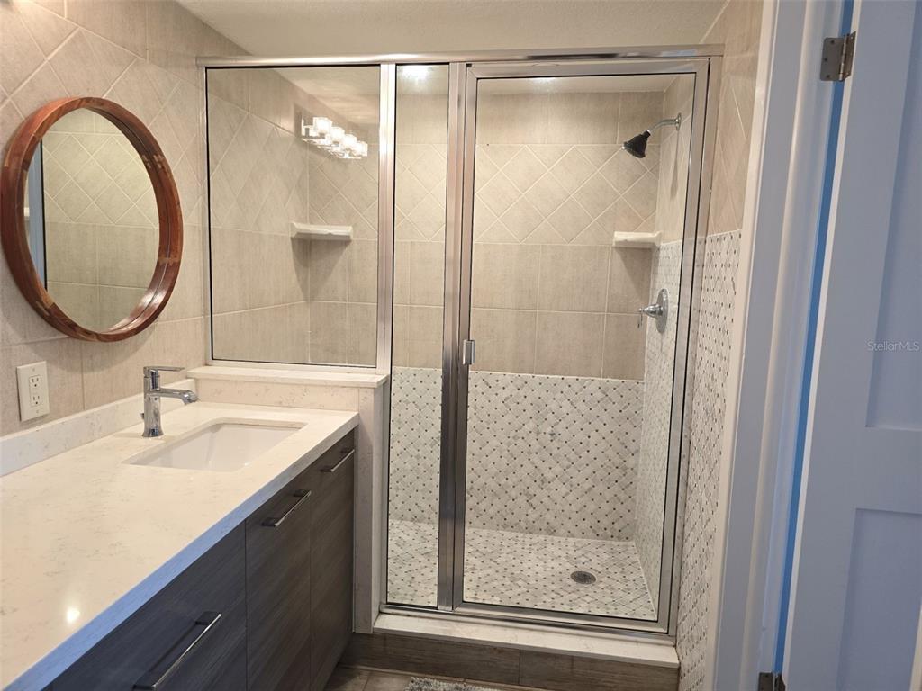 17408 Gulf Boulevard, Unit 1003 Redington Shores, FL 33708 - Photo 22 of 28 a bathroom with a granite countertop sink a mirror and a shower