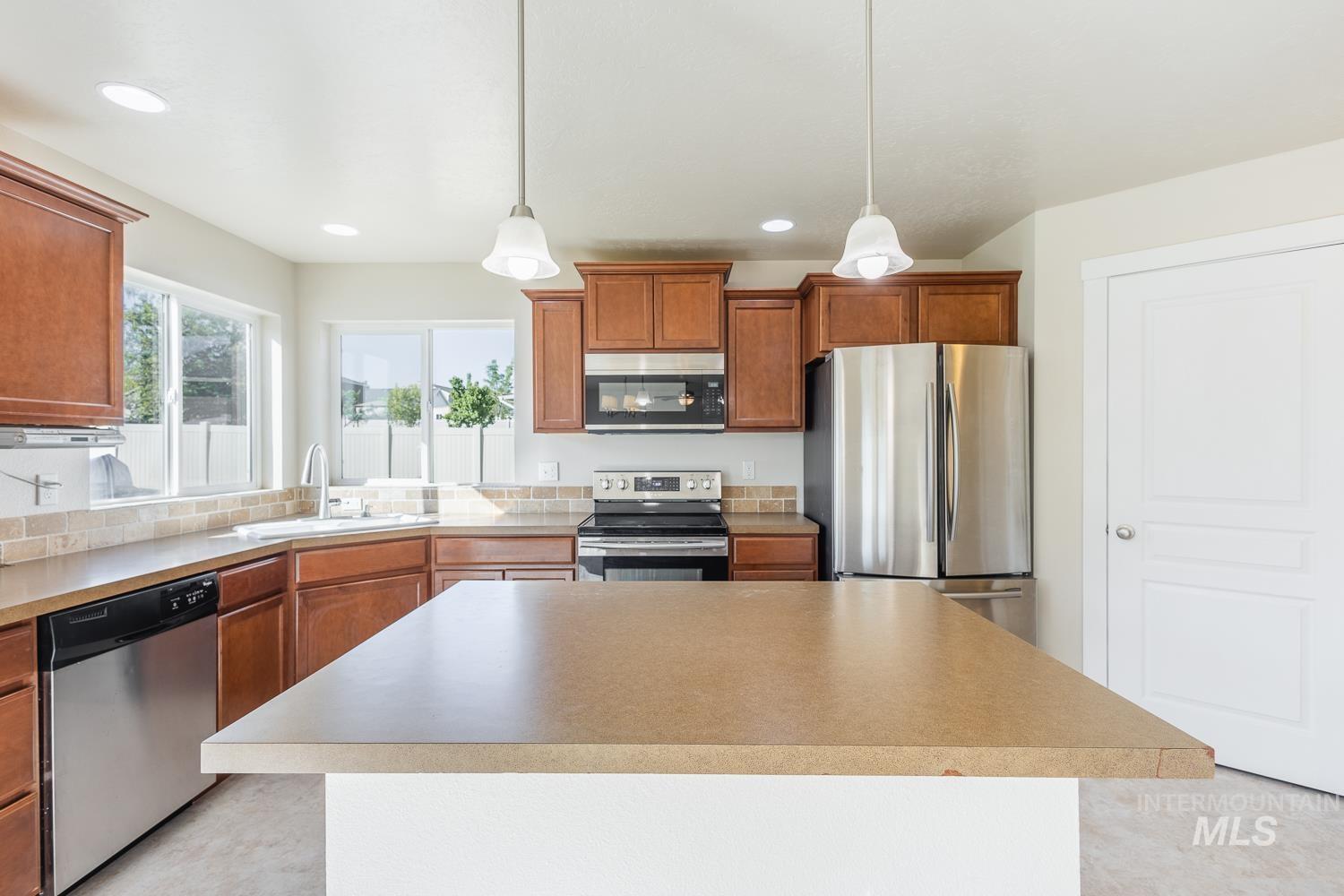 14253 Moreno Drive Caldwell, ID 83607 - Photo 11 of 48 Kitchen featuring an island with a solid surface countertop, stainless steel appliances, wood cabinetry, tile backsplash, and recessed lighting