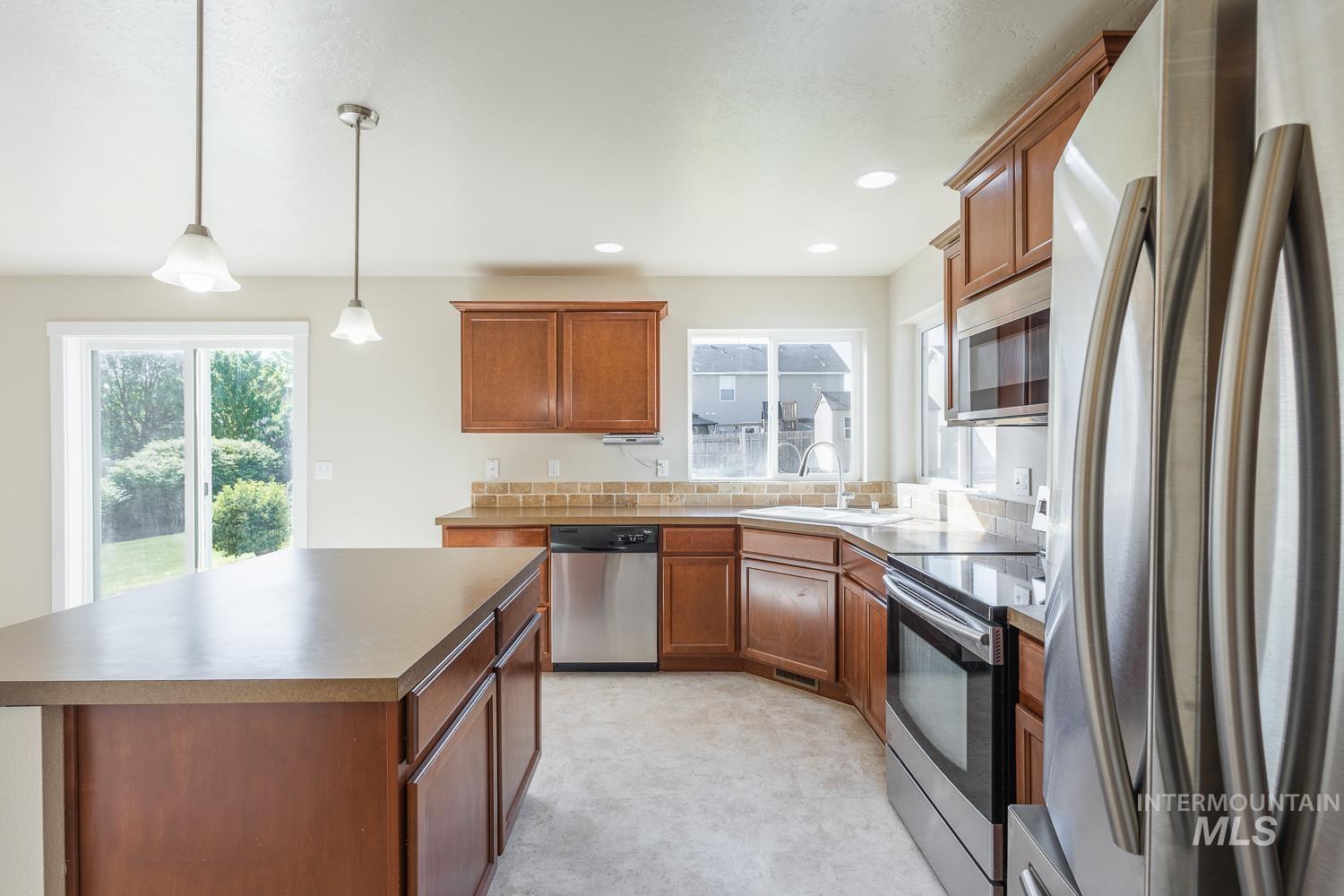 14253 Moreno Drive Caldwell, ID 83607 - Photo 12 of 48 Kitchen featuring wood cabinetry, stainless steel appliances, a corner sink, and a multi-toned tile backsplash