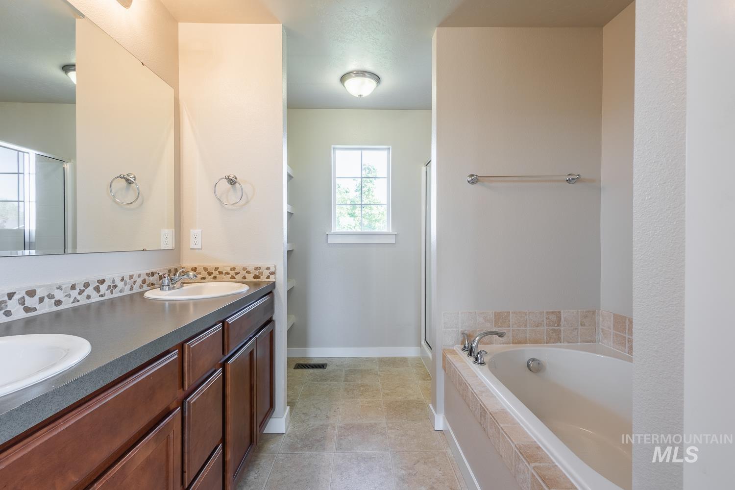 14253 Moreno Drive Caldwell, ID 83607 - Photo 19 of 48 Bathroom featuring a dual-sink vanity with wood-finish cabinetry and a stone-look countertop, a tiled soaking tub, a separate shower enclosure, and built-in shelving
