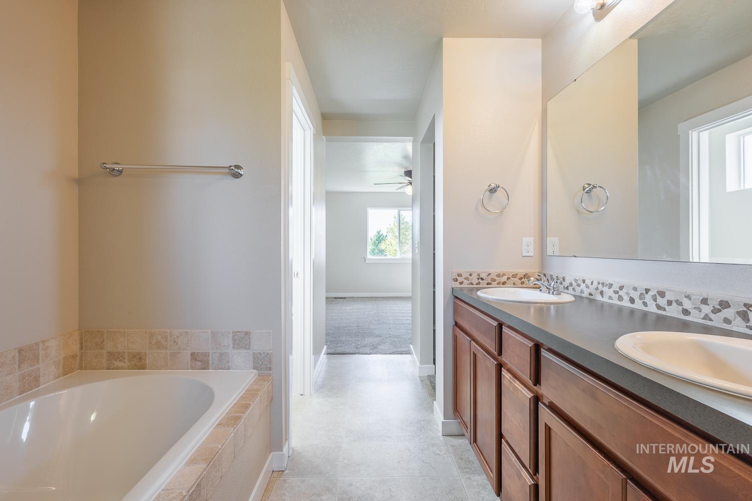 14253 Moreno Drive Caldwell, ID 83607 - Photo 20 of 48 Bathroom featuring a built-in tub with tile surround, dual vanity with undermount sinks, and a full-width mirror