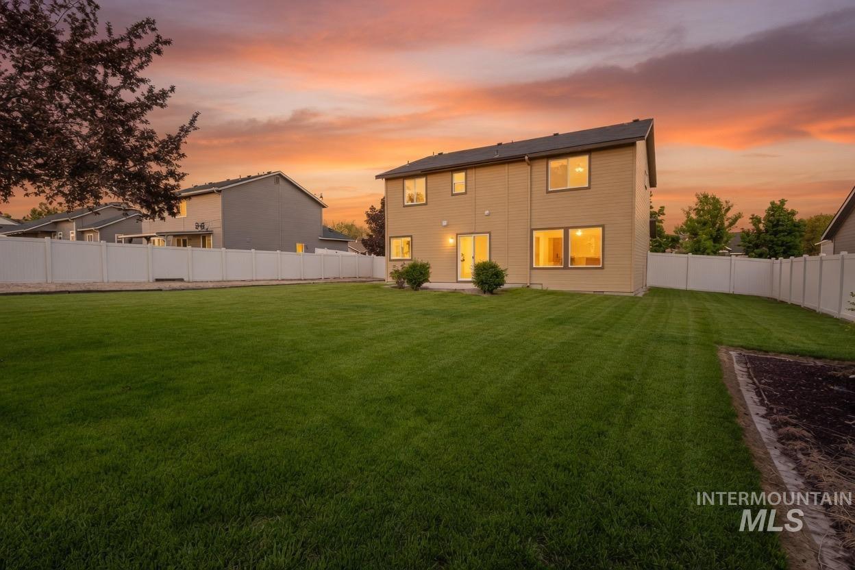 14253 Moreno Drive Caldwell, ID 83607 - Photo 2 of 48 Expansive backyard featuring a manicured lawn, a vinyl privacy fence, a concrete patio, and a two-story residence with light-colored siding