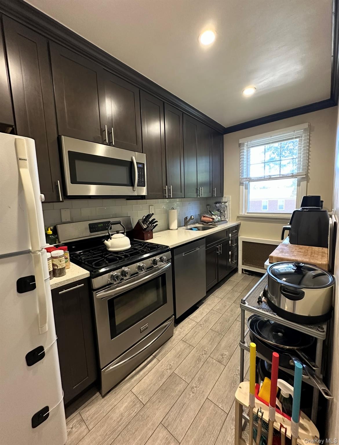 100 Cedar Street, Unit A21 Dobbs Ferry, NY 10522 - Photo 6 of 12 Kitchen with appliances with stainless steel finishes, decorative backsplash, light wood-style floors, recessed lighting, and ornamental molding