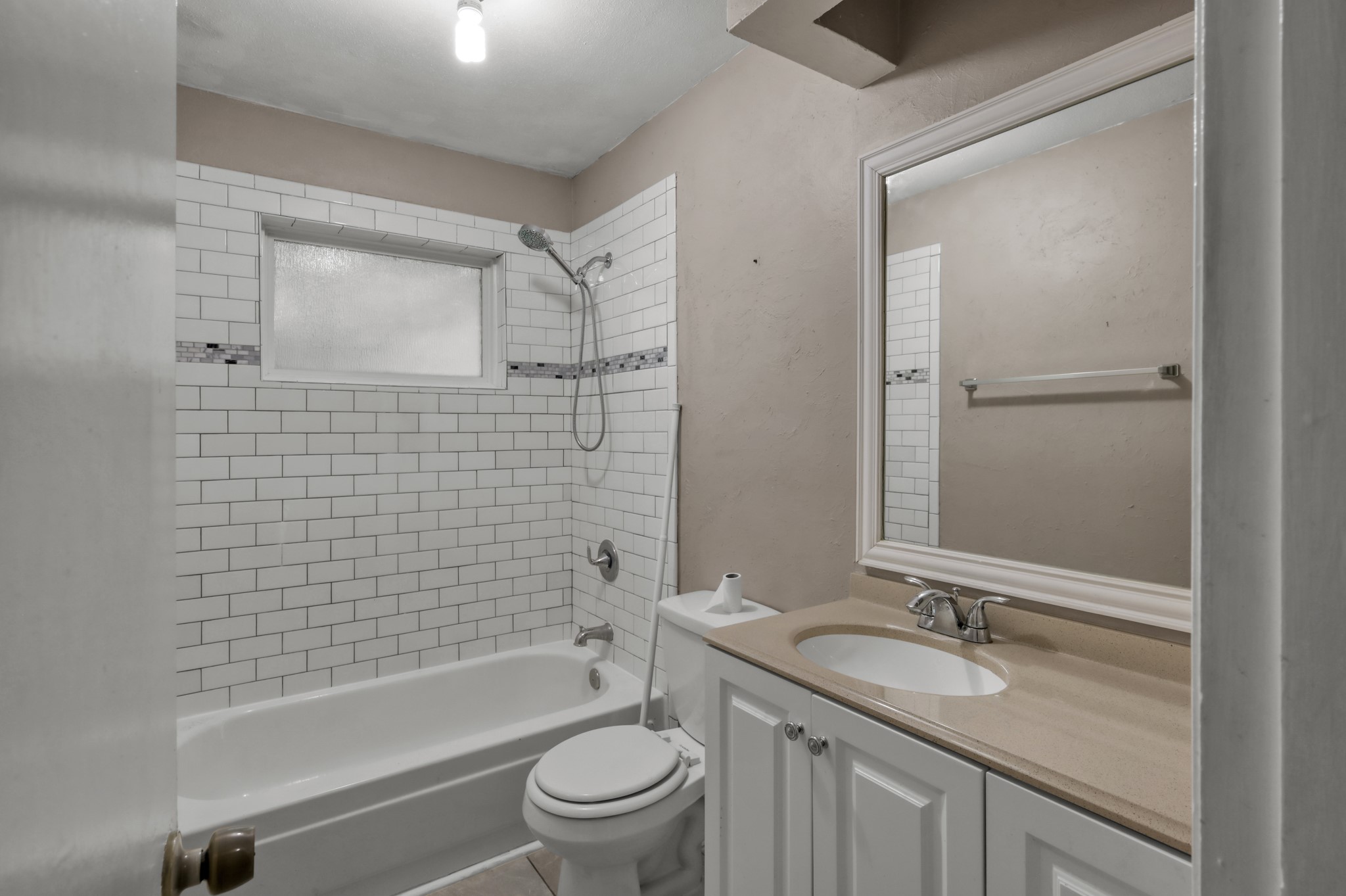 12015 Fallbrook Drive Houston, TX 77065 - Photo 22 of 29 This bathroom features a classic design with white subway tile on the bathtub walls, a neutral-colored countertop, and a clean white vanity with a modern faucet. It's well-lit and has a small window for natural light.