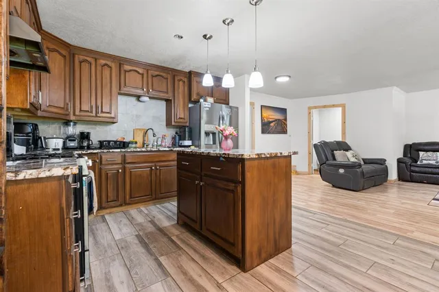 a kitchen with stainless steel appliances granite countertop wooden cabinets a sink a stove a dining table and chairs