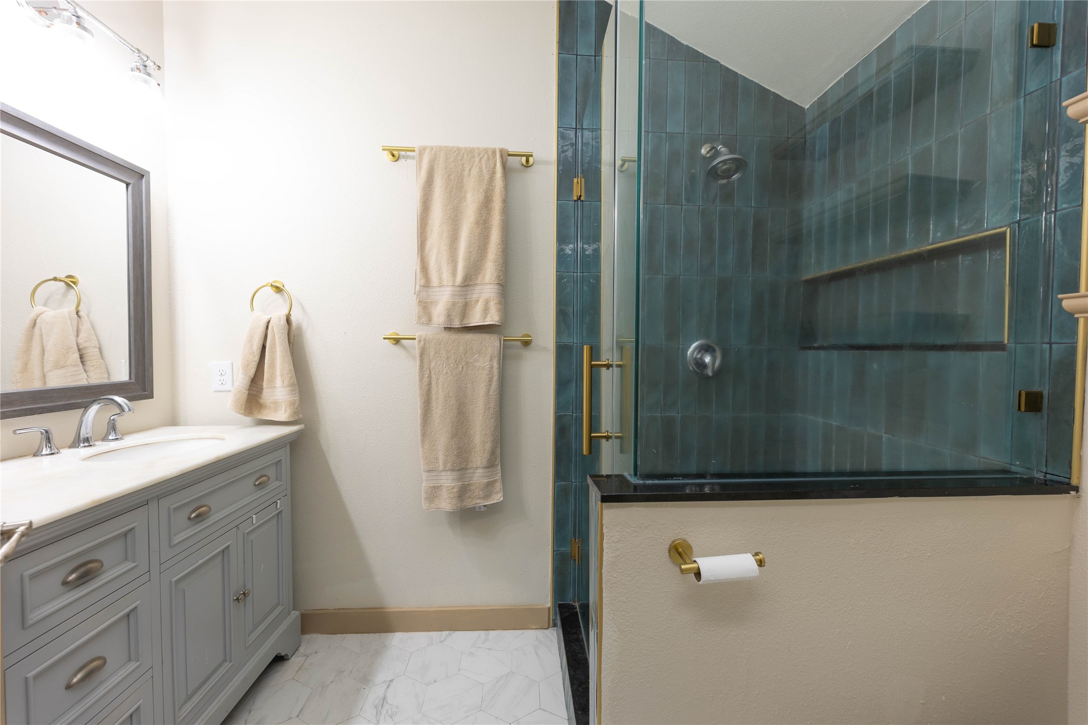 8007 Capitol Street Houston, TX 77012 - Photo 17 of 25 This bathroom features a modern design with a glass-enclosed shower, blue subway tiles, and a built-in shelf. It has a stylish gray vanity with a marble countertop and dual sinks. Neutral walls and gold fixtures add a touch of elegance.