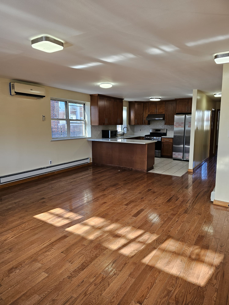 a living room with stainless steel appliances wooden floors and kitchen view
