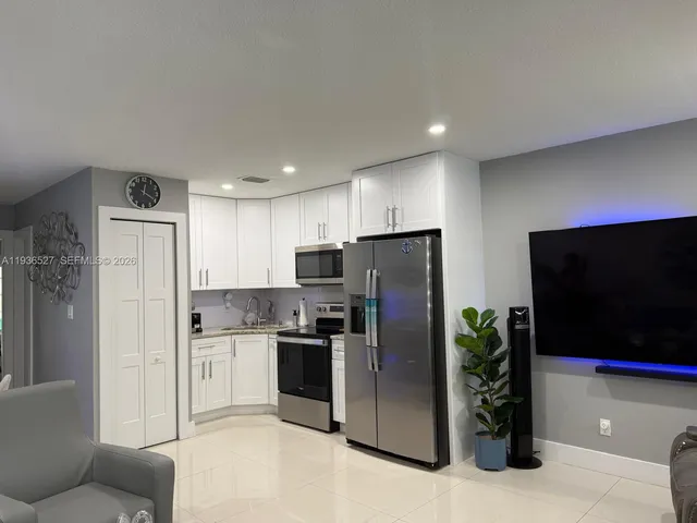 a kitchen with stainless steel appliances kitchen island granite countertop a refrigerator a stove a sink a washer and dryer with wooden floor