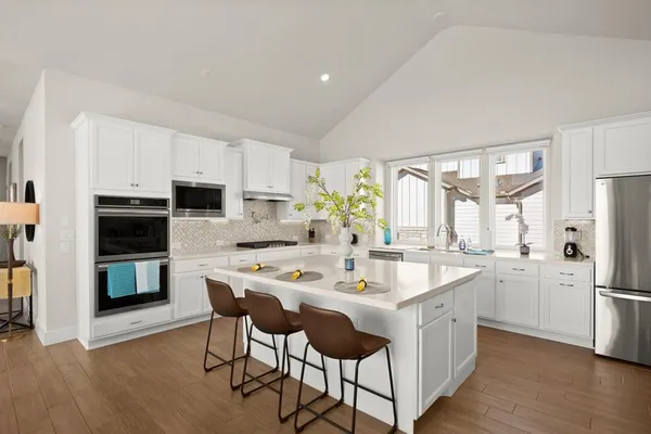 a kitchen with stainless steel appliances kitchen island granite countertop a table chairs refrigerator and microwave