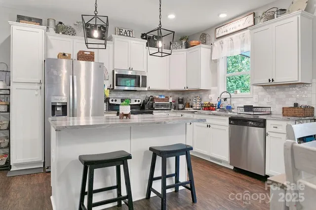 a kitchen with stainless steel appliances granite countertop a refrigerator a sink dishwasher a stove and white cabinets with wooden floor