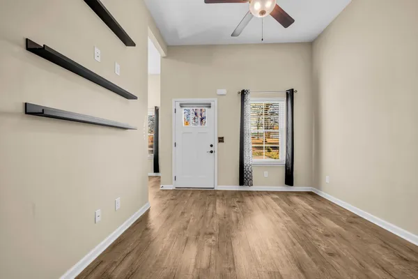 an empty room with wooden floor chandelier fan and windows