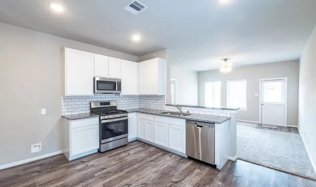 a kitchen with stainless steel appliances granite countertop a stove top oven a sink and white cabinets