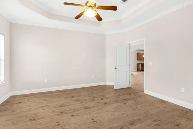an empty room with wooden floor ceiling fan and windows