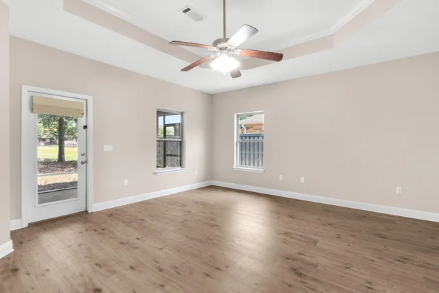 an empty room with wooden floor chandelier fan and windows