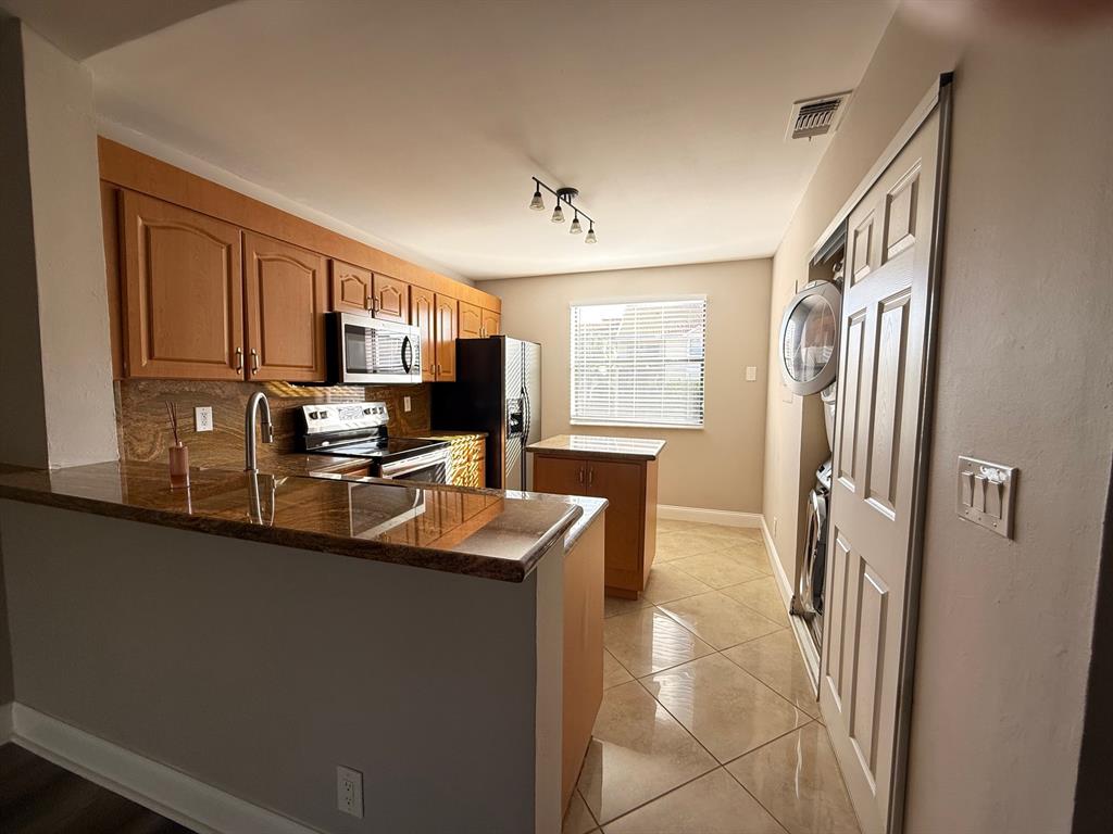 5781 Riverside Drive, Unit 201 Coral Springs, FL 33067 - Photo 3 of 23 a kitchen with stainless steel appliances granite countertop a refrigerator a sink dishwasher a stove top oven a dining table and chairs with wooden floor