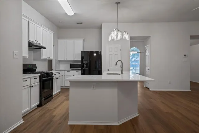 a kitchen with stainless steel appliances a chandelier a stove a sink dishwasher a refrigerator and white cabinets with wooden floor