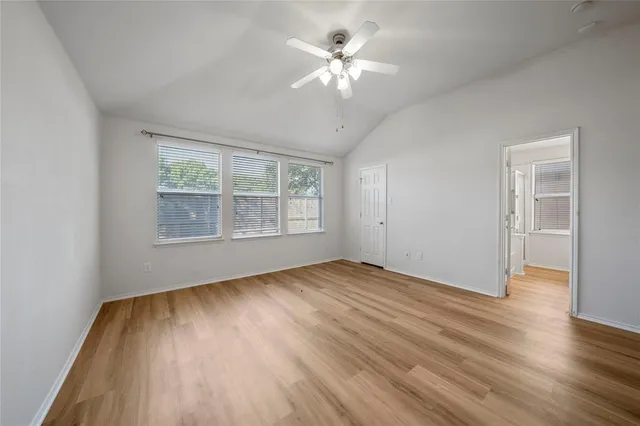 an empty room with wooden floor chandelier fan and windows